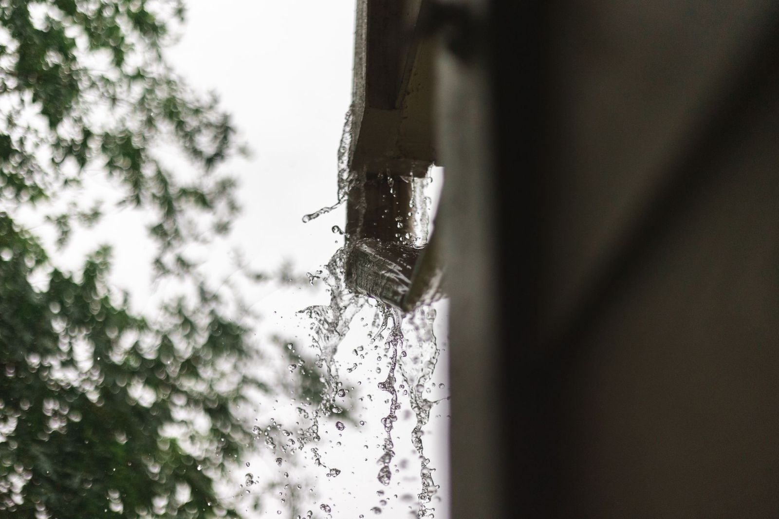 Pluie ruisselant d'une gouttière zinc sur une toiture en tuiles